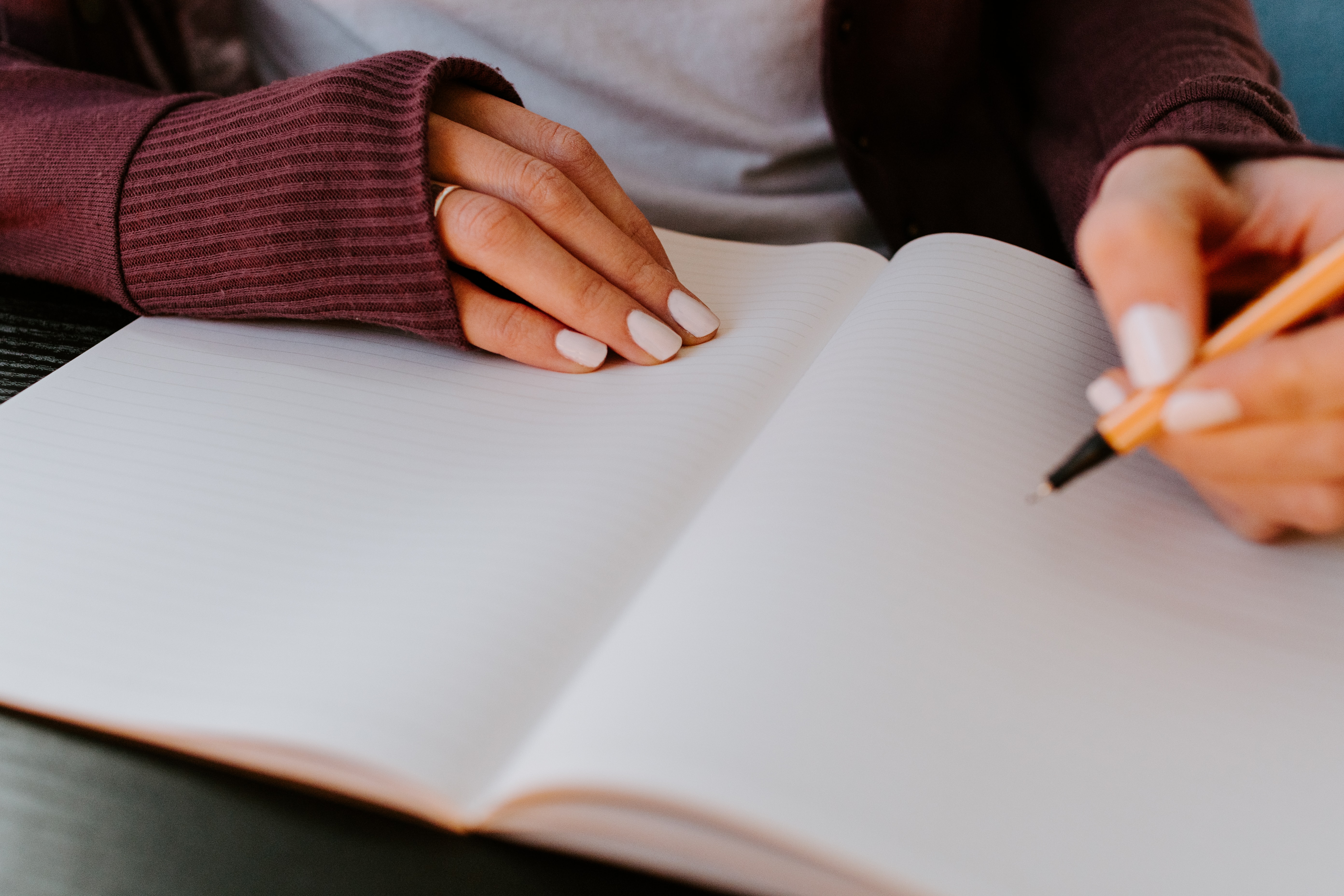 Focus sur les mains d'une personne tenant un stylo et écrivant dans un cahier